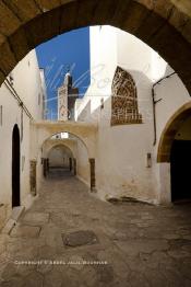 Image du Maroc Professionnelle de  Dans une rue des Habous, la succession des balèvres, moulure, arches, portiques et autres éléments décoratifs, projetent les visiteurs dans l’ardeur avec un élan de force et de fierté d’une époque révolue. Conçu par les architectes Auguste Cadet et Edmond Brion d’après l’ébauche d’un premier plan-masse dû à Albert Laprade, le quartier fait partie des endroits les plus pittoresques de Casablanca, il fut La construction n’avait commencé qu’après la première guerre mondiale. Situé près du Palais Royale, ce joyau architectural fait partie du patrimoine architectural de la ville, Samedi 8 Novembre 2008. Au centre le minaret de La mosquée Ben Youssef. (Photo / Abdeljalil Bounhar)
